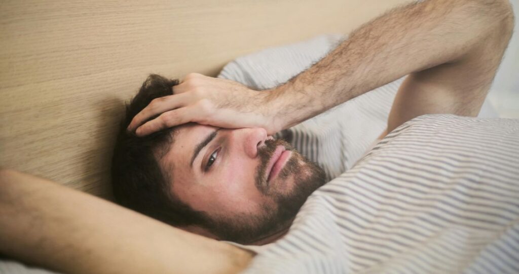 Image of a man in bed, with his hand on his head