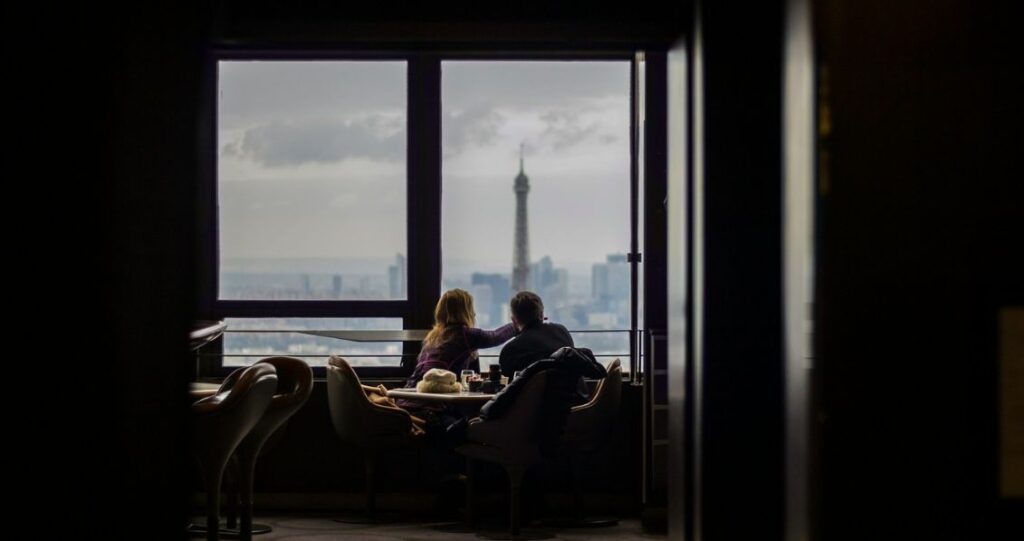 Couple sitting by the window in a hotel room in paris with a view of the Eiffel Tower